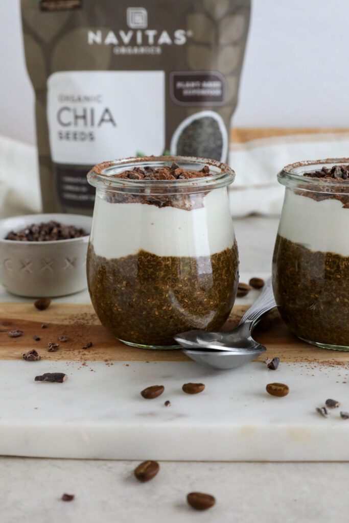 Viral Tiramisu Chia Pudding served in weck jars with two spoons surrounded by cacao nibs and coffee beans 