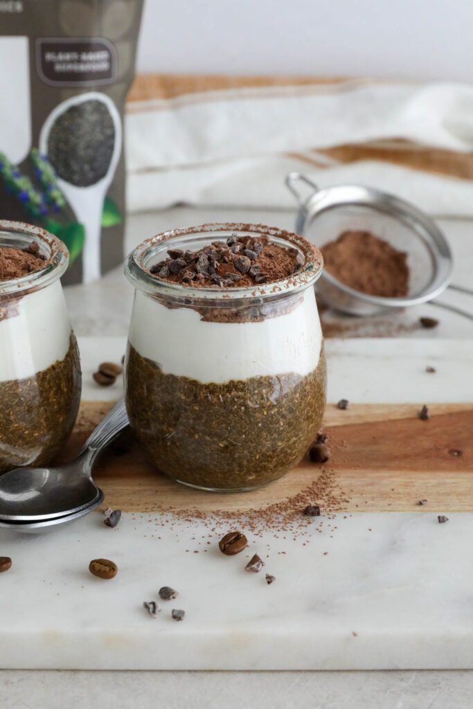 Viral Tiramisu Chia Pudding served in weck jars with two spoons surrounded by cacao nibs and coffee beans 