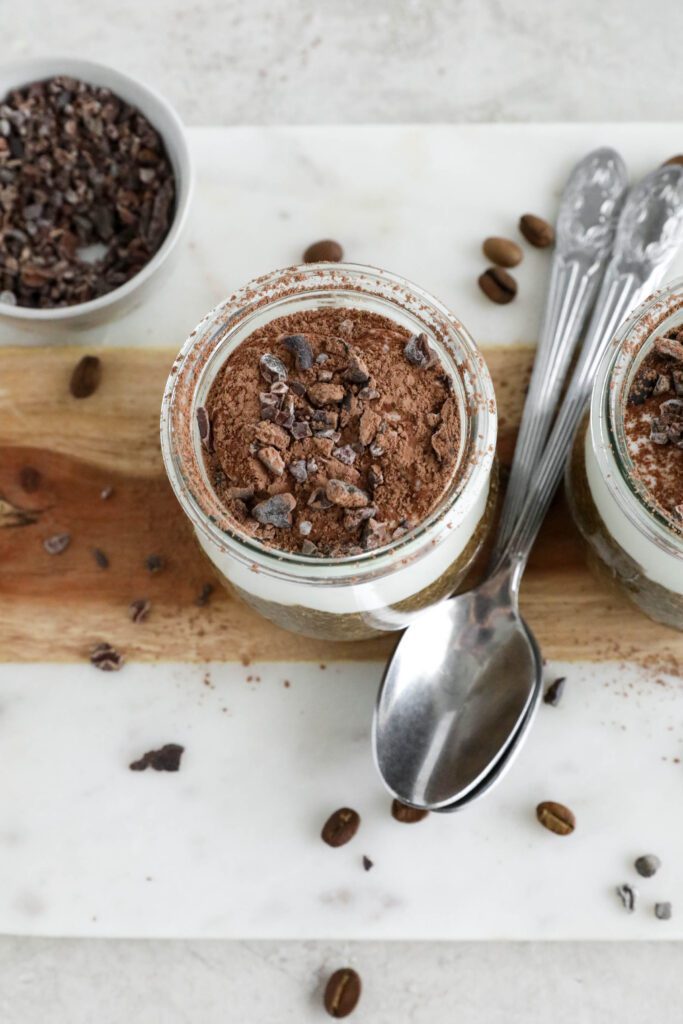 Viral Tiramisu Chia Pudding served in weck jars with two spoons surrounded by cacao nibs and coffee beans 