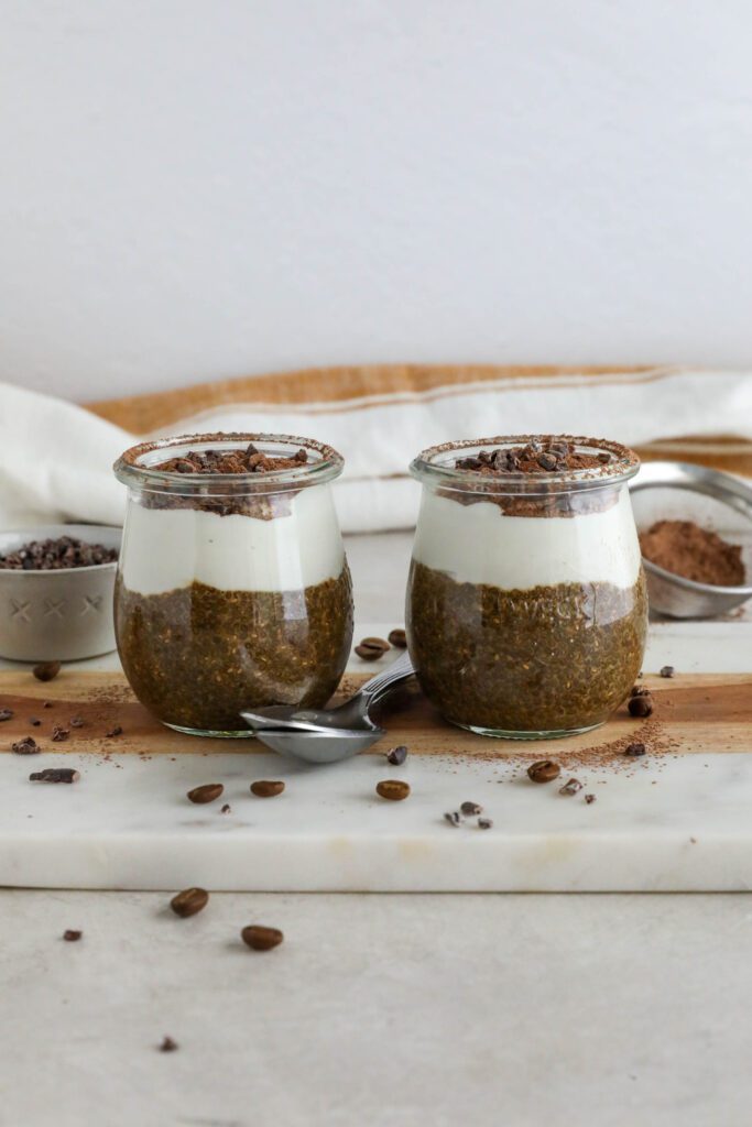 Viral Tiramisu Chia Pudding served in weck jars with two spoons surrounded by cacao nibs and coffee beans 