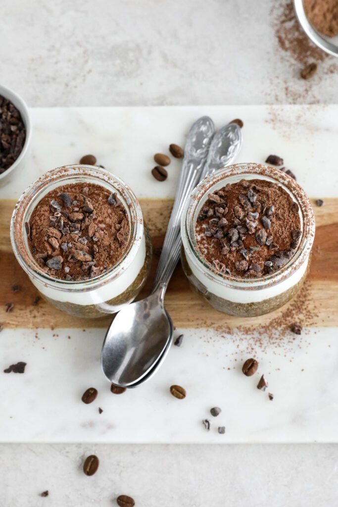 Viral Tiramisu Chia Pudding served in weck jars with two spoons surrounded by cacao nibs and coffee beans 