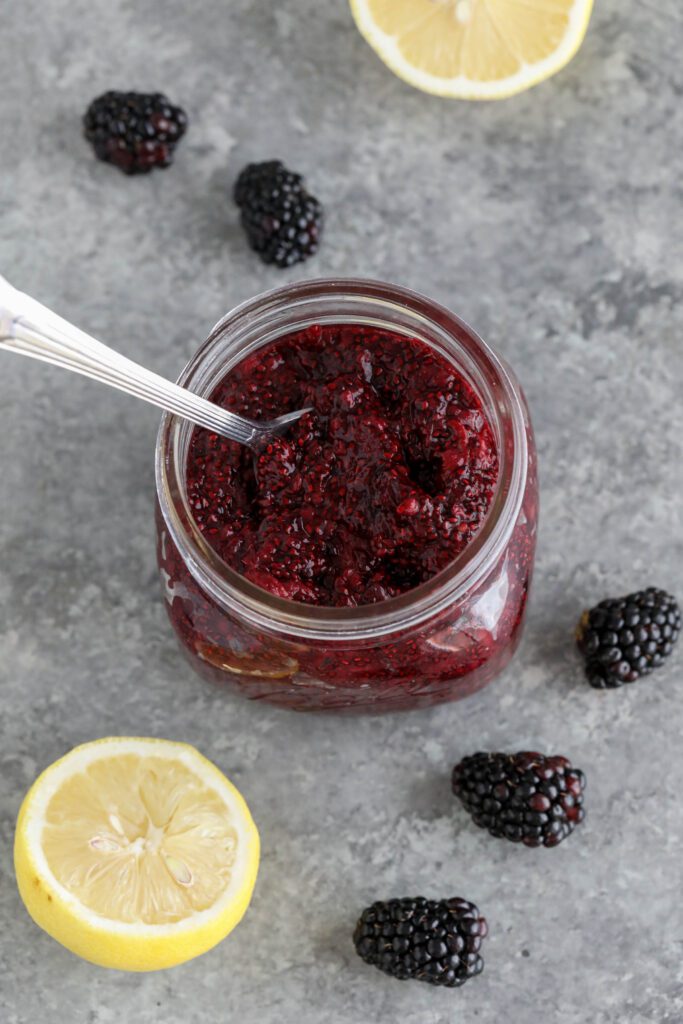 Blackberry Chia Jam in mason jar with spoons with blackberries and lemons scattered