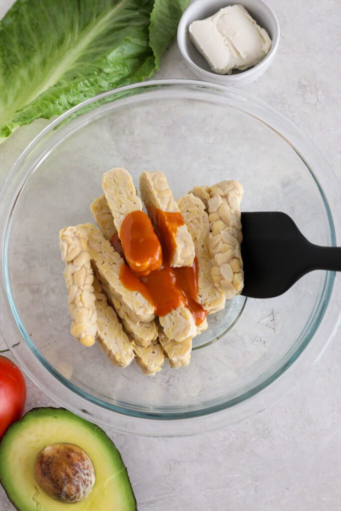 tempeh sliced with buffalo sauce on top with spatula 