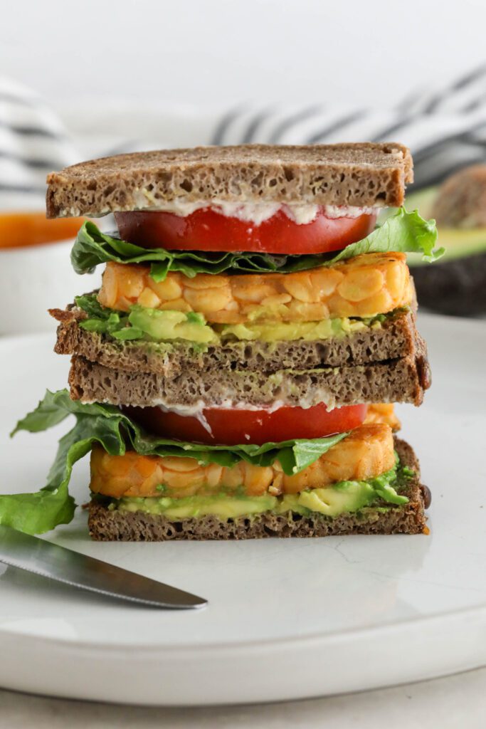 Buffalo Tempeh Sandwich stacked on white plate