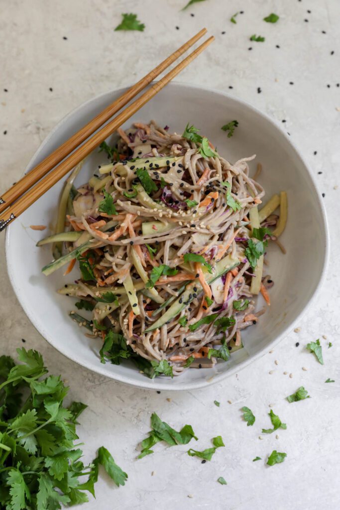 Cold SunButter Soba Noodles served in bowl with chopsticks topped with cilantro and sesame seeds