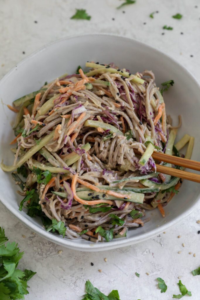 Cold SunButter Soba Noodles served in bowl with chopsticks topped with cilantro and sesame seeds