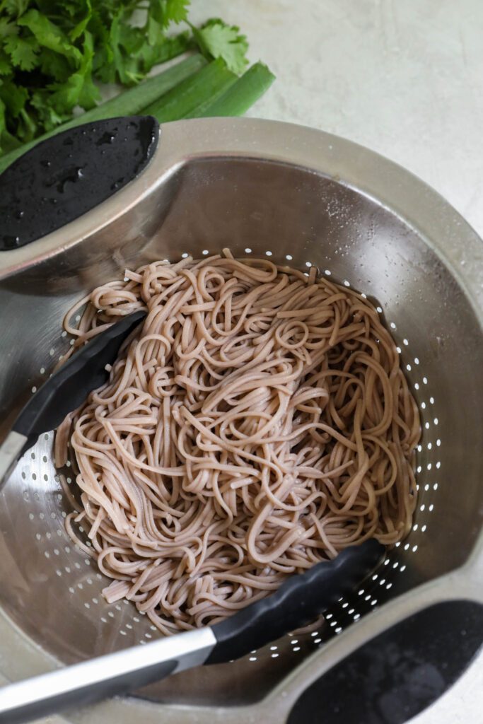Soba Noodles in colander with tongs and cilantro on the side
