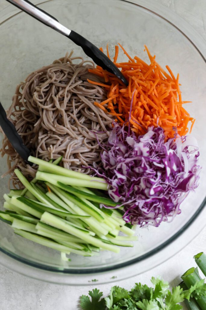 Soba noodles in bowl with vegetables with tongs with cilantro on side