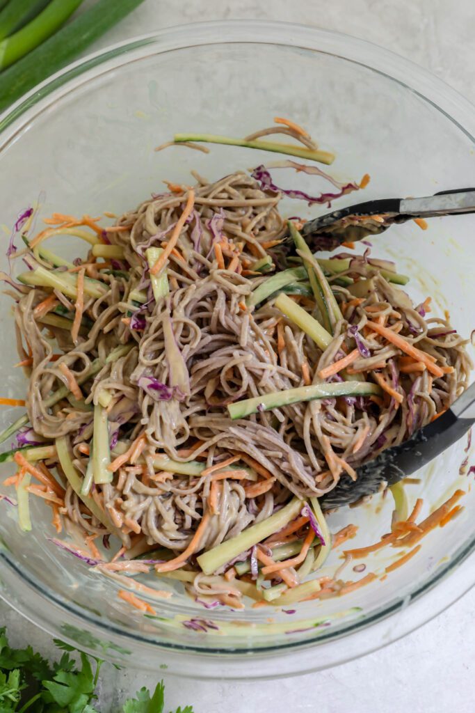 Cold SunButter Soba Noodles mixed together in bowl with tongs