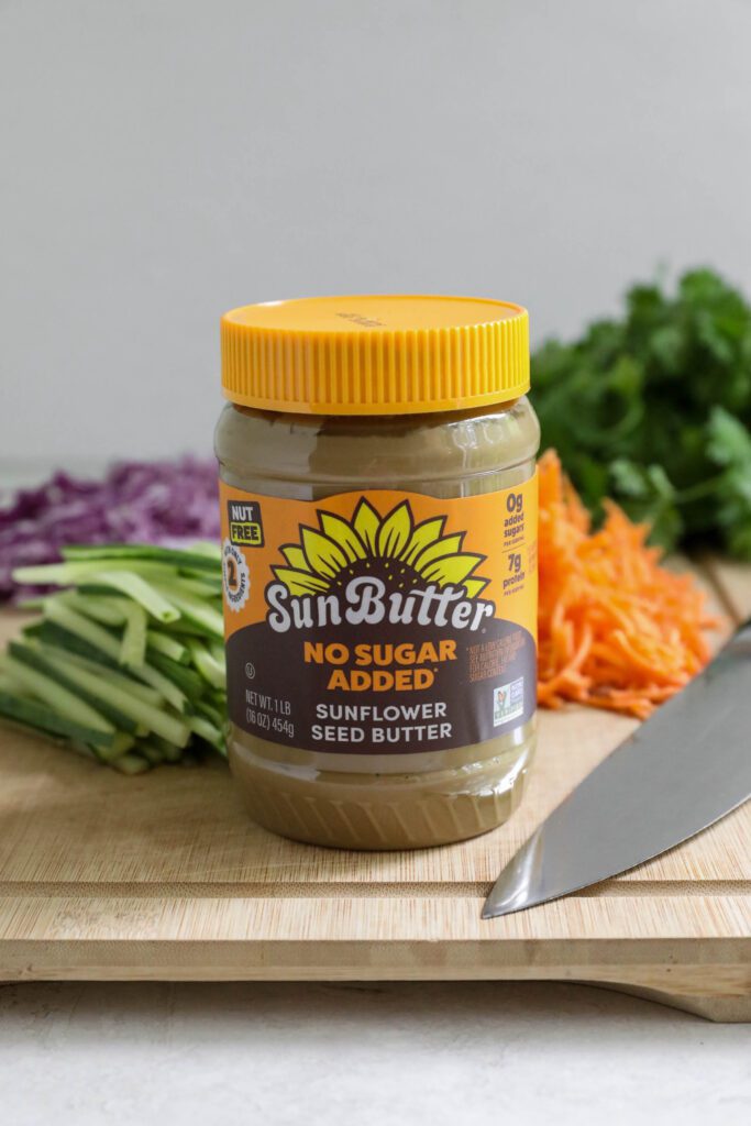 SunButter jar with carrots, cucumber, cabbage, and cilantro on cutting board with knife