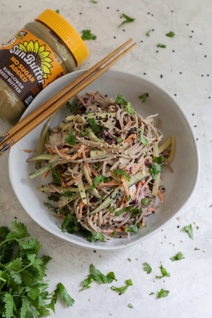 Cold SunButter Soba Noodles served in bowl with chopsticks topped with cilantro and sesame seeds