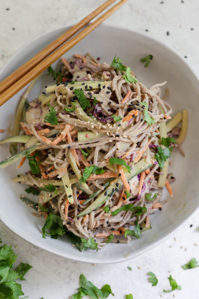 Cold SunButter Soba Noodles served in bowl with chopsticks topped with cilantro and sesame seeds