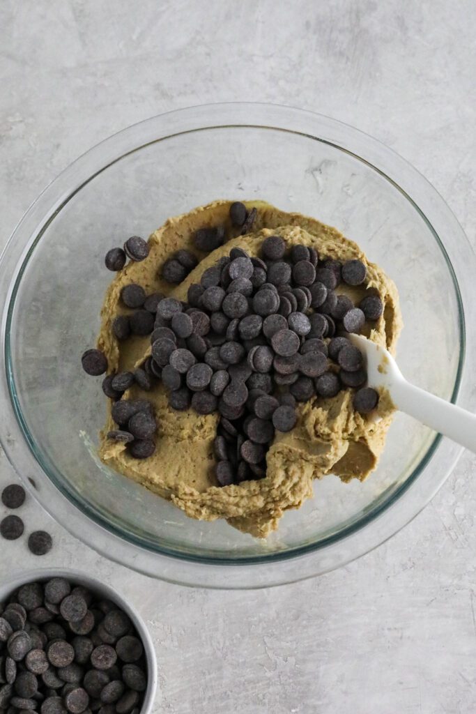 chocolate chip protein cookie batter in bowl topped with chocolate chips and spatula