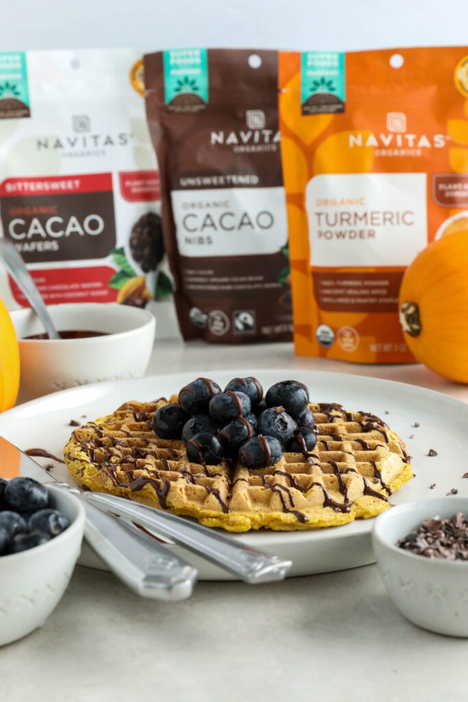 Pumpkin Turmeric Waffles served on plate topped with blueberries, cacao nibs, and chocolate drizzle 