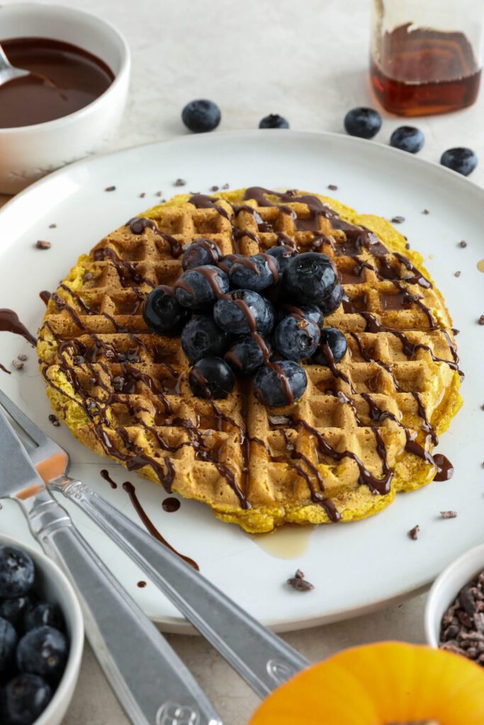 Pumpkin Turmeric Waffles served on plate topped with blueberries, cacao nibs, and chocolate drizzle 