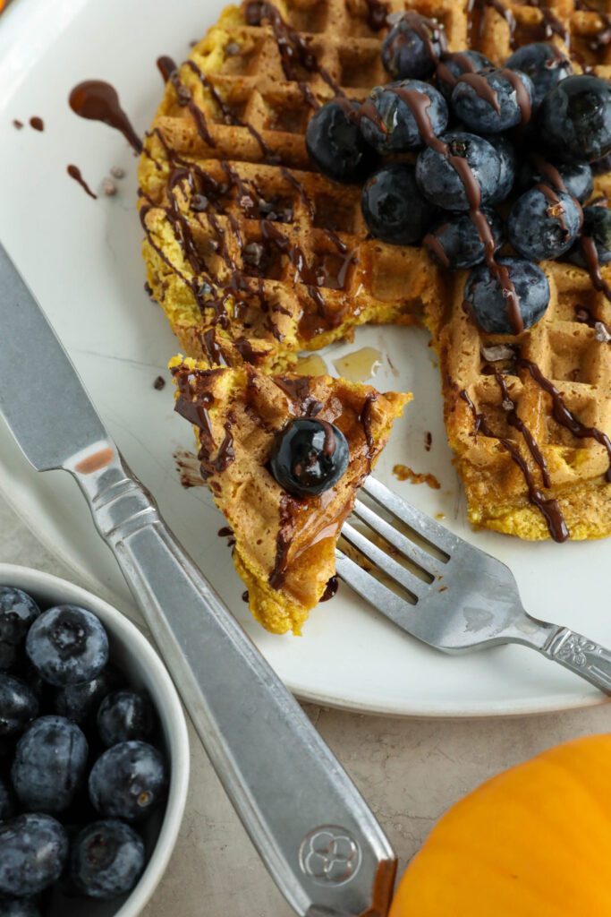 Pumpkin Turmeric Waffles served on plate topped with blueberries, cacao nibs, and chocolate drizzle 