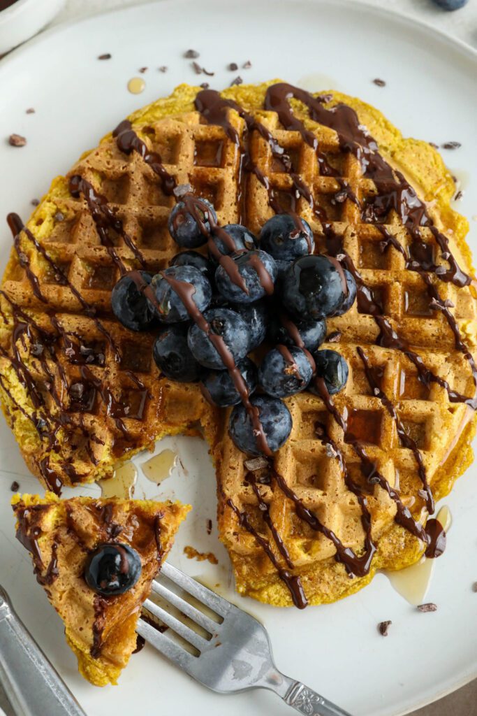 Pumpkin Turmeric Waffles served on plate topped with blueberries, cacao nibs, and chocolate drizzle 