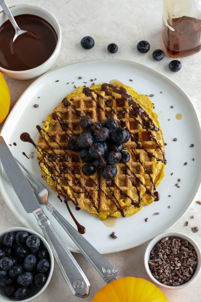 Pumpkin Turmeric Waffles served on plate topped with blueberries, cacao nibs, and chocolate drizzle 