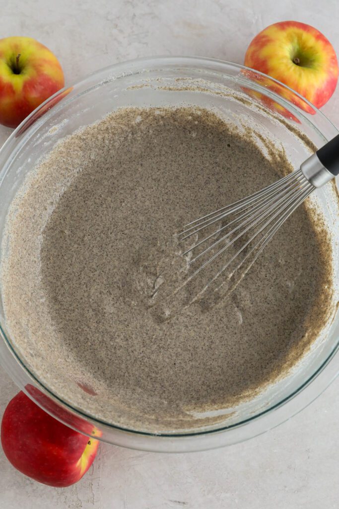 vegan apple pie pancake buckwheat batter in bowl with whisker surrounded by apples 