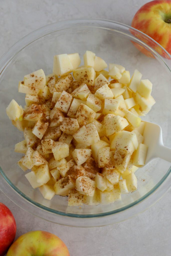 diced apples in bowl topped with cinnamon and maple syrup with spatula 