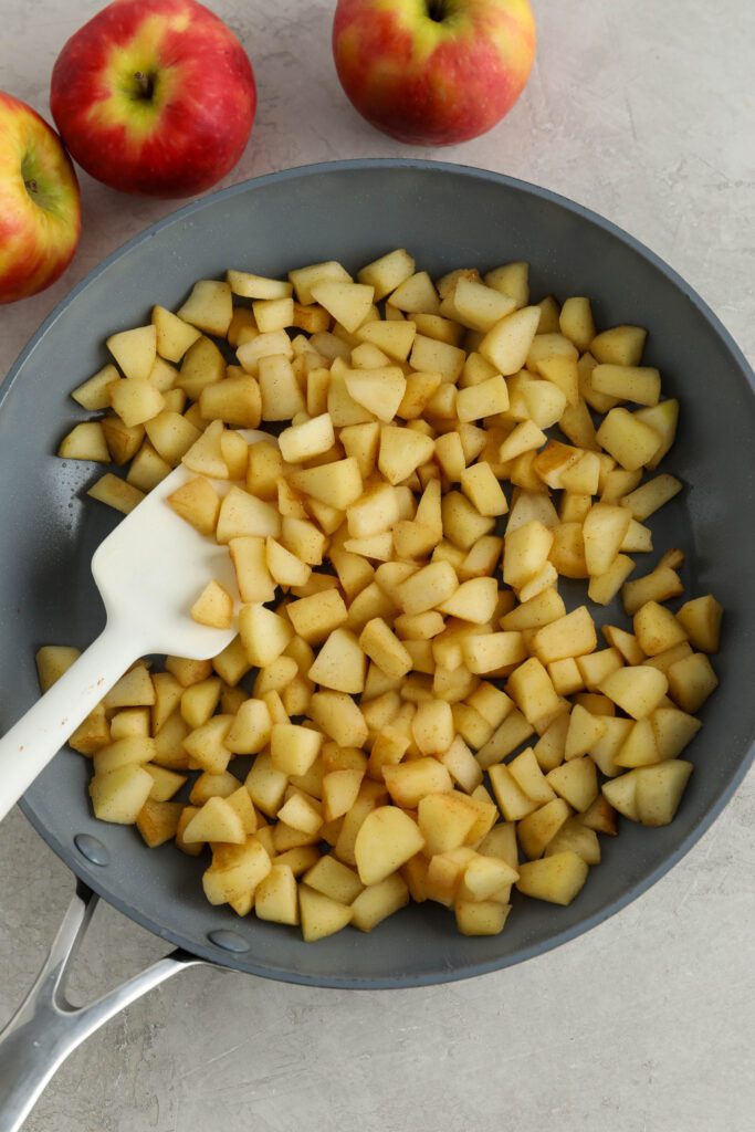 sautéed apples in pan with spatula surrounded by apples 