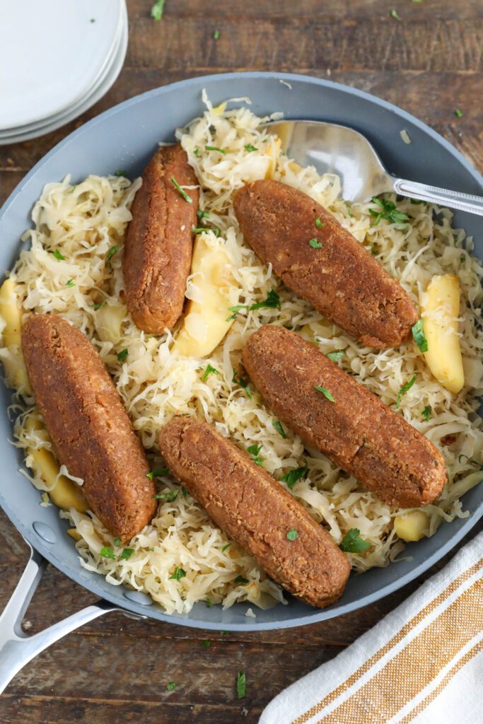 Vegan Bratwurst with Sauerkraut in pan with spoon topped with parsley