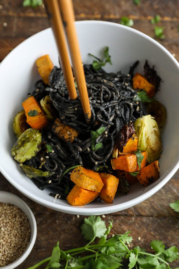 Black Sesame Noodle Bowl served in bowl topped with cilantro and sesame seeds with chopsticks