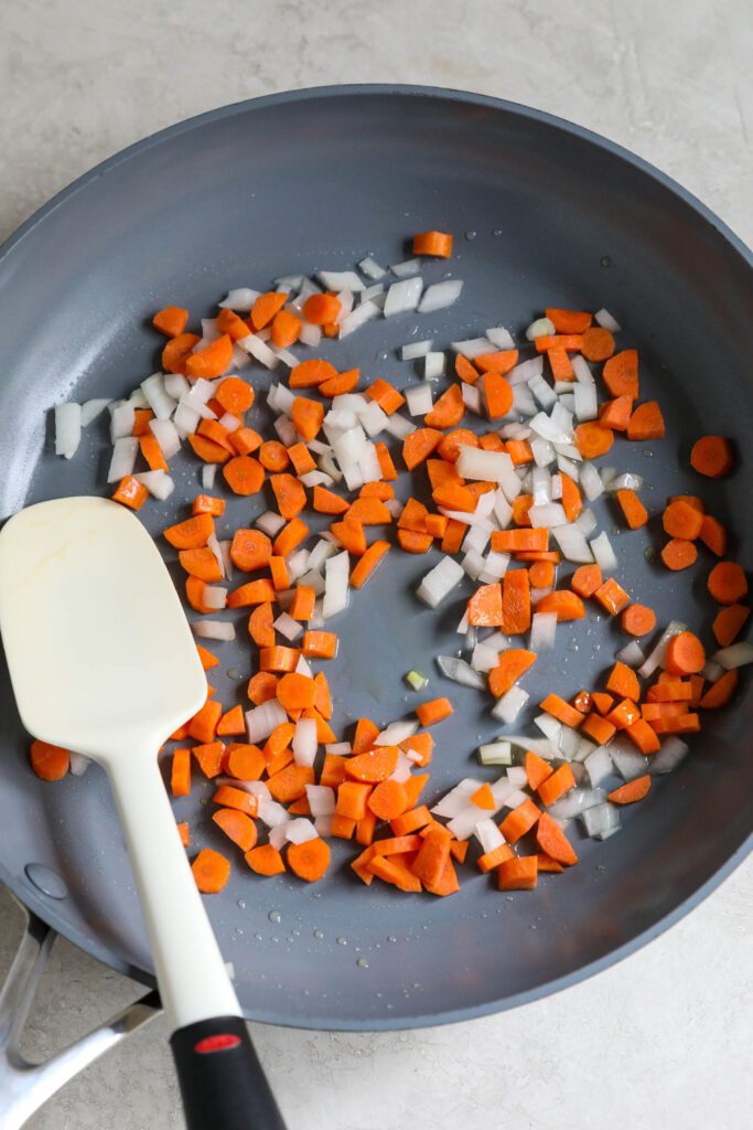 diced white onion and carrots in skillet with spatula