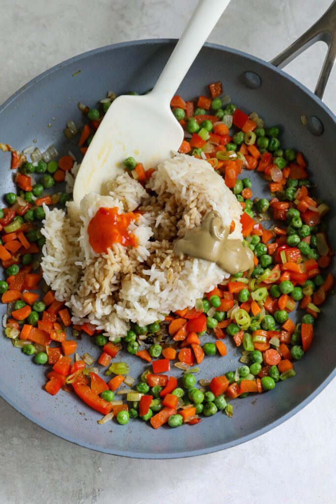 rice, chili garlic sauce, and SunButter added to sautéed vegetables in pan with spatula