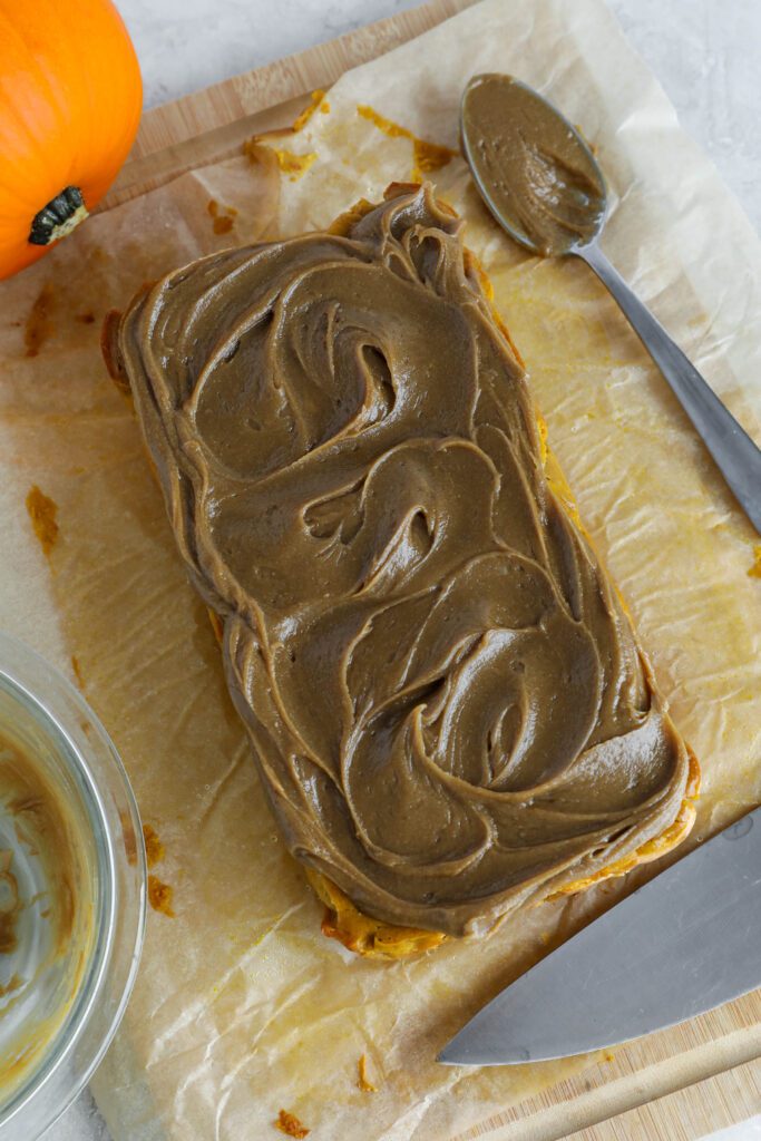 SunButter frosting on top of pumpkin cheesecake on parchment paper with knife
