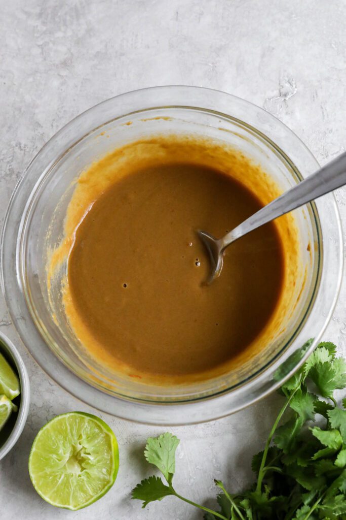 SunButter sauce mixed in glass bowl with spoon surrounded by lime and cilantro 