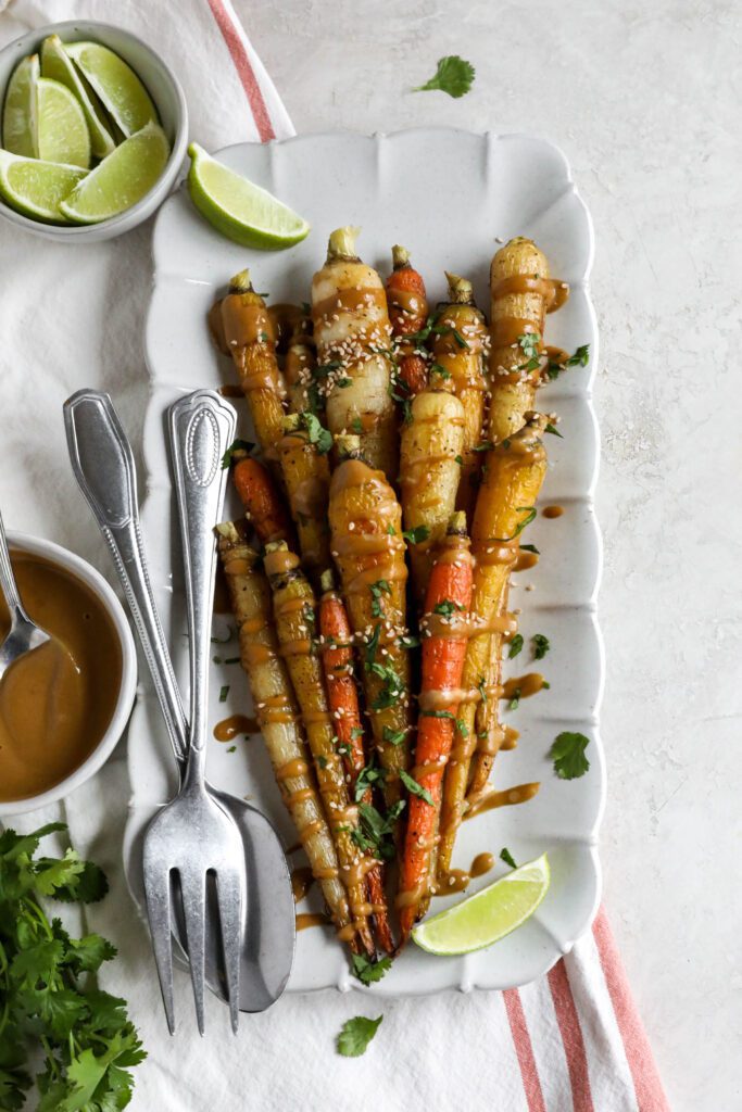Rainbow Roasted Carrots with SunButter Sauce served on rectangular platter with fork and spoon and lime 