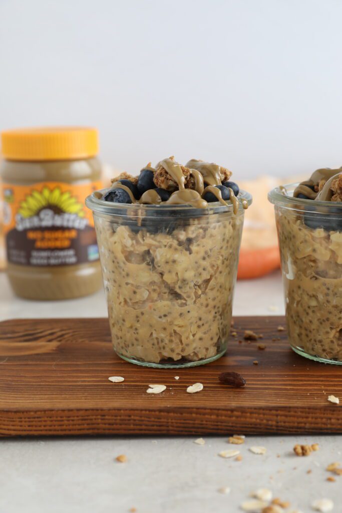 Carrot Cake SunButter Overnight Oats served in mason jars on wooden board topped with blueberries, granola, and SunButter 