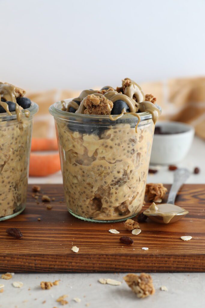 Carrot Cake SunButter Overnight Oats served in mason jars on wooden board topped with blueberries, granola, and SunButter 