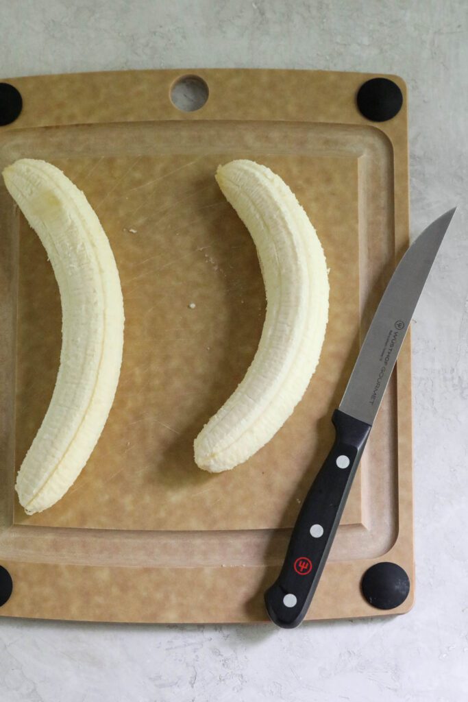 two bananas on a wooden cutting board with a knife