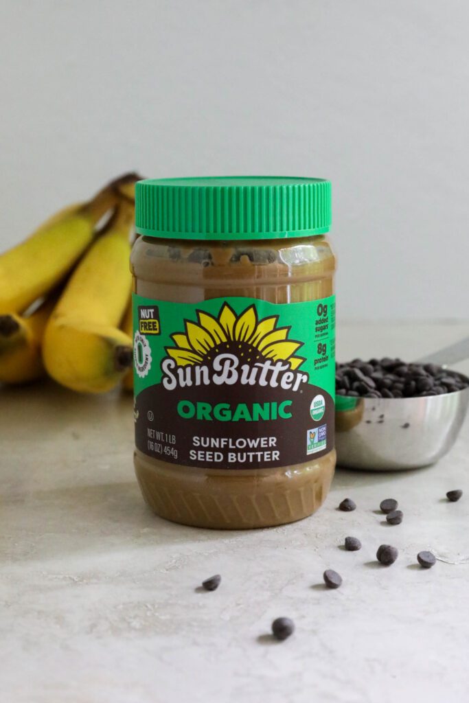 Jar of Organic SunButter with bananas and chocolate chips behind it